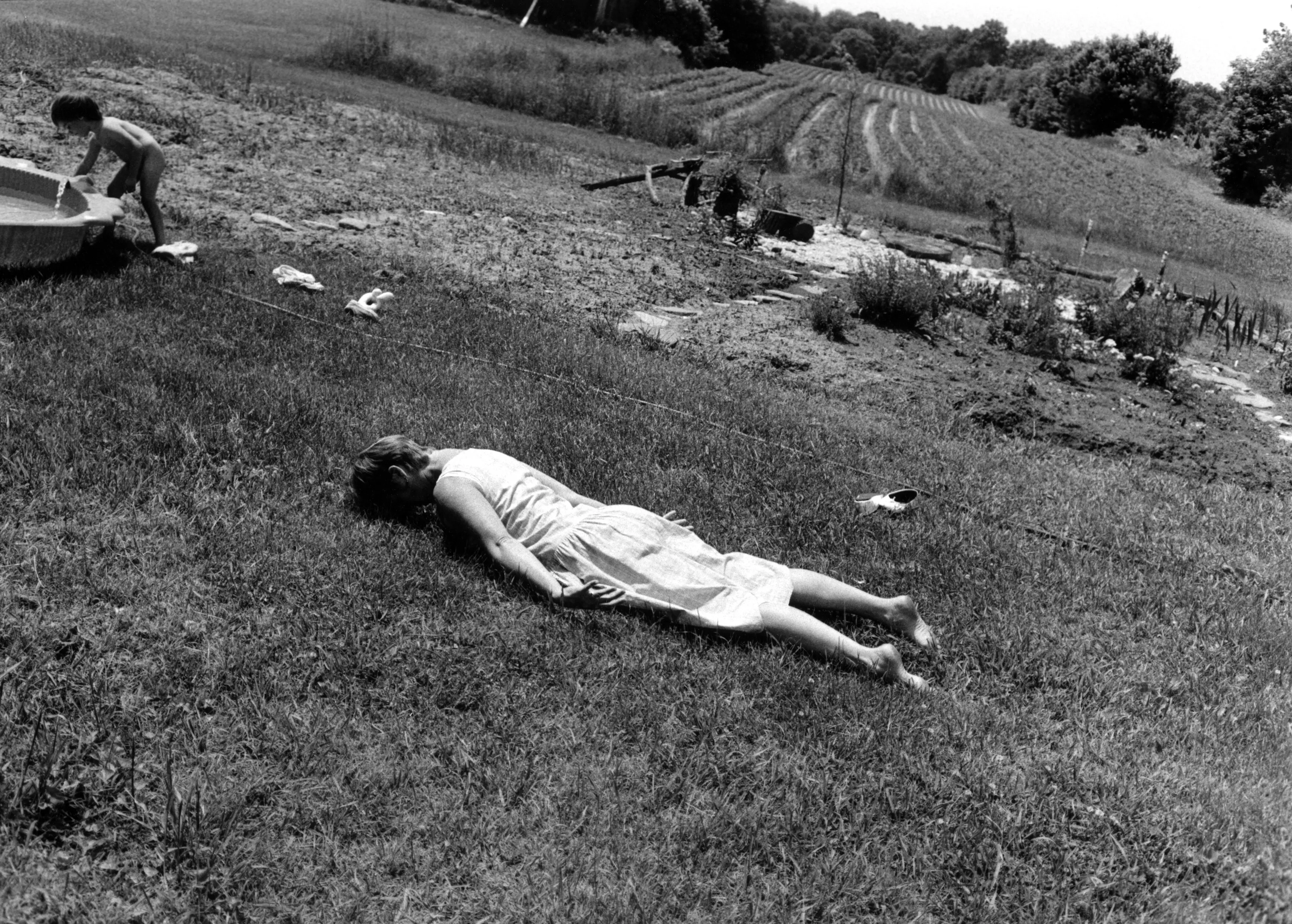 A black and white image of 2 kids outside with the girl facedown on the floor